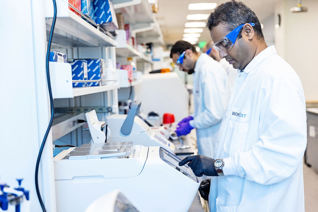 BiomEdit scientists in lab coats and safety glasses working at lab equipment
